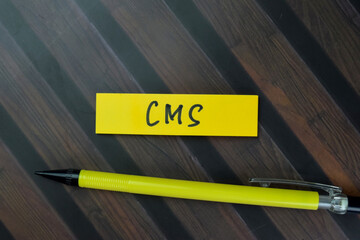 Concept of CMS write on sticky notes isolated on Wooden Table.