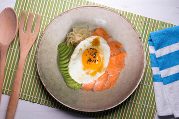 Teriyaki salmon donburi with fried egg, avocado, onion, red pepper and other vegetables. Typical Japanese dish.