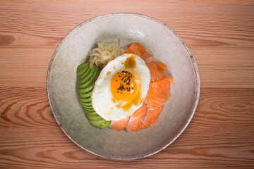 Teriyaki salmon donburi with fried egg, avocado, onion, red pepper and other vegetables. Typical Japanese dish.