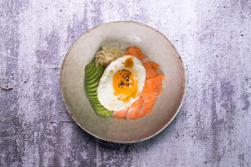 Teriyaki salmon donburi with fried egg, avocado, onion, red pepper and other vegetables. Typical Japanese dish.