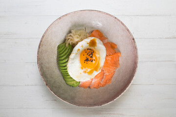 Teriyaki salmon donburi with fried egg, avocado, onion, red pepper and other vegetables. Typical Japanese dish.