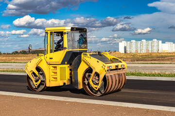 Vibratory road roller lays asphalt on a new road under construction. Close-up of the work of road machinery. Construction work on the construction of urban highways.
