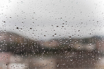Close-up of a window on a grey rainy day with the glass full of raindrops falling down
