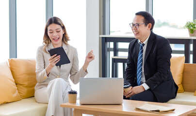 Fototapeta premium Millennial Asian young successful professional female businesswoman and male businessman colleague in formal suit sitting working with laptop notebook computer together in company office living room