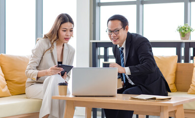 Millennial Asian young successful professional female businesswoman and male businessman colleague in formal suit sitting working with laptop notebook computer together in company office living room