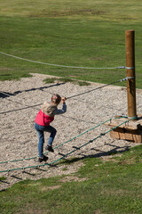 Sur une aire de jeu une petite fille marche souple sur une échelle  agrippée  à une corde
