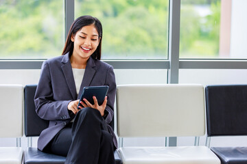 Millennial Asian happy cheerful successful professional female businesswoman employee in formal suit sitting smiling on chair take break holding using touchscreen tablet computer reading data news