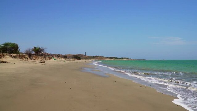 Motion video of the yellow sand of beautiful Zorritos beach in Tumbes, Peru, on a sunny day with the tide coming in.