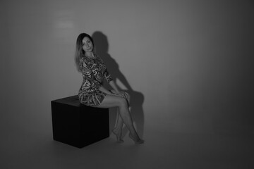 Slender woman with beautiful legs sitting on a cube in black and white