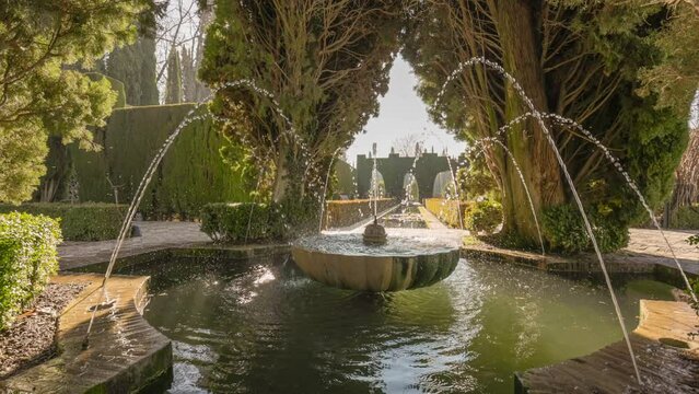 Fountain surrounded by trees in Gardens of the Generalife in Alhambra. Granada, Spain. Camera moves between trees to pond with fountain in Generalife Gardens. Slow motion HDR gimbal shot