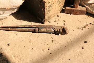 Old working tools for the house, a rusty adjustable wrench, a large hammer, a shabby tool box on a concrete floor in a barn.