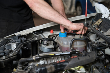Car mechanic hands replacing antifreeze container. Mechanics workshop.