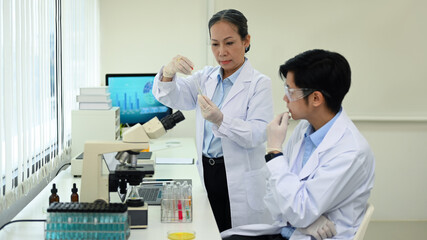 Two professional scientist conducting experiment with test tubes and microscope in research laboratory