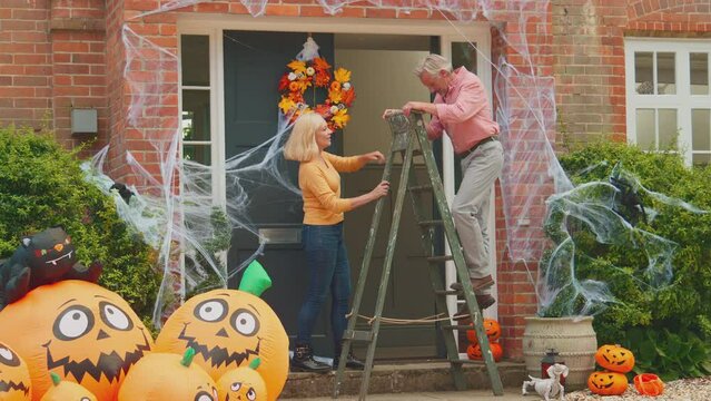 Grandparents with stepladder putting up halloween decorations ready for grandchildren to come trick or treating - shot in slow motion