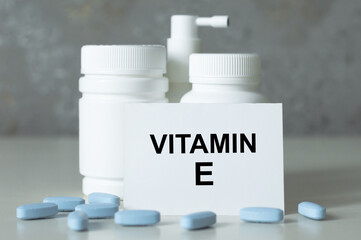 VITAMIN E text on the card on the table next to there are white cans of medicine and scattered tablets