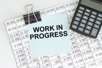 WORK IN PROGRESS text on a blue card clip to a sheet with numbers next to the calculator