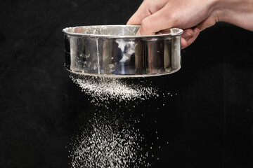 a man sifts flour through a sieve on a black background