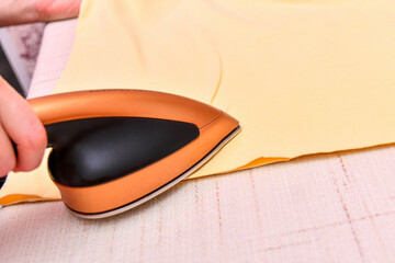 A woman irons yellow clothes after washing with a small iron.