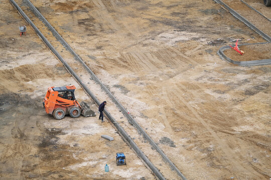 Excavator And Workers Laying Curbs At A Parking Lot Construction Site