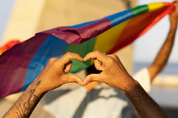 Hands making heart sign in front of rainbow flag.