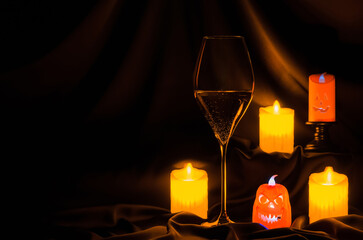 A glass of white wine with small halloween lantern and blurred focus candle on dark cloth background. Halloween dinner party concept.