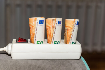 Euro banknotes stuck in an electric power strip at home,concept of increase energy cost, home finances and saving money on electricity consumption.Selective focus.