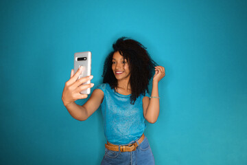 Social media influencer streaming video with her smartphone. Afro hairstyle black touching taking selfie.