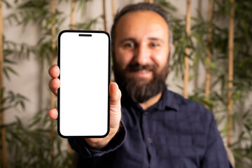 Modern smartphone mock up, caucasian bearded young man holding and showing modern smartphone mock up. Selective focus on hand. White blank screen for recommendation concept idea photo with copy space.