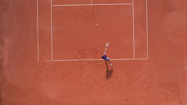 Male athlete plays tennis on a professional court during competition tournament, slow motion aerial view