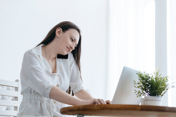 smiling woman working on a laptop and talking on her smartphone.