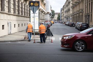 Pair of workers at work near a manhole cover in the city with a car passing in the street