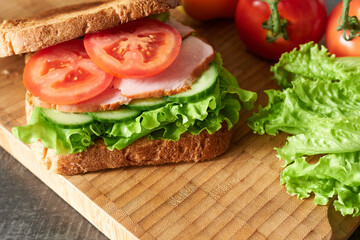 A tomato and ham sandwich close-up on a wooden background. The concept is a student's breakfast.