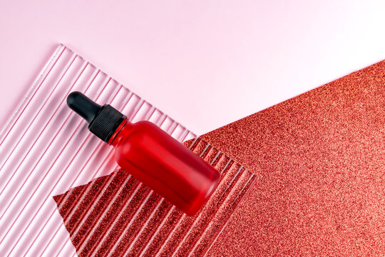 Product photo. Mockup of face serum bottle with blank label on pink and glittering red background. Beauty concept, facial skin care