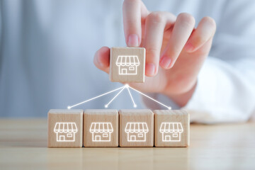 Franchise Business marketing concept. Hand holding franchise store icon on wooden block with line network connection to another store.	
