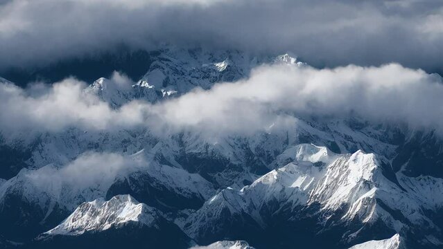 Clouds Over Himalaya Mountains View From Flight. Aerial drone footage over Alps. Massive rocky peaks covered with snow. Dramatic moving clouds covering hill landscape. High altitude summer tourism.