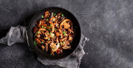 Roasted mushrooms with onion in frying pan on a dark background. Copy space. Top view.
