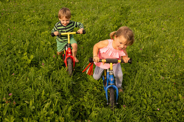 Little girl and boy riding bike in the grass and having fun
