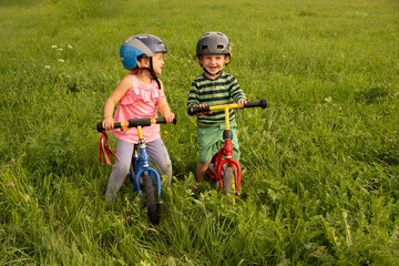 Little girl and boy having fun riding a bike in the grass