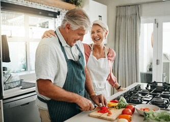 Senior couple, cooking and having fun while preparing a healthy food with vegetables for a vegan meal in the kitchen at home while laughing and having fun. Funny old man and woman helping with dinner