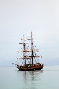 Vertical shot of two-masted wooden ship sailing in the sea under cloudy sky