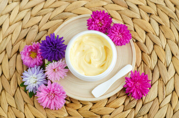Obraz na płótnie Canvas Yellow facial mask (banana face cream, shea butter hair mask, body butter) and purple flowers. Natural skin and hair care concept. Top view, copy space.