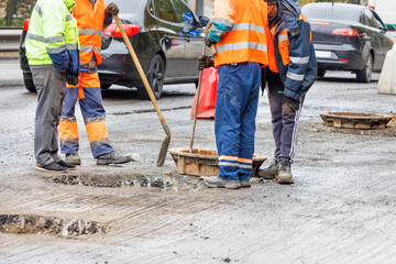 A group of road workers are repairing the sewer manhole system on the carriageway against the background of passing cars in blur. - obrazy, fototapety, plakaty