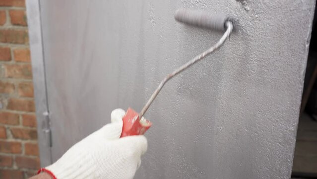 men's gloved hand paints the metal garage door with a roller. 
