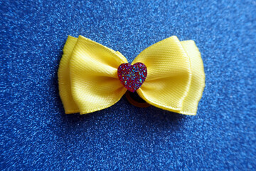 a yellow bow with a red shiny heart lies on a blue shiny background.  accessories.  decorations for dogs