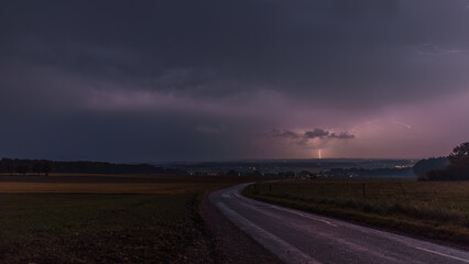 Gewitterhimmel mit Gewitterwolken und grellen Blitz und eine strasse im Vordergrund.