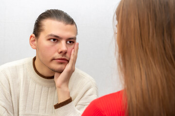 emotional portrait of a man listening to a woman on a light background, covers his mouth with his hand. Concept: bewilderment, boredom, unexpected news.