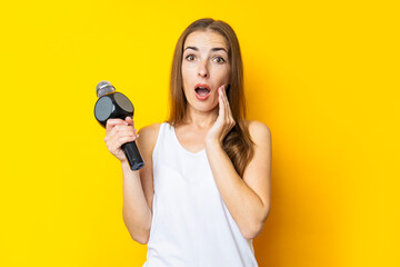 Surprised young woman holding a microphone on a yellow background. Reporter or journalist concept