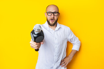 Young man is interviewing holding a microphone in front of him on a yellow background