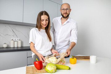 Young woman and young man putting out fresh vegetables from the bag in the kitchen