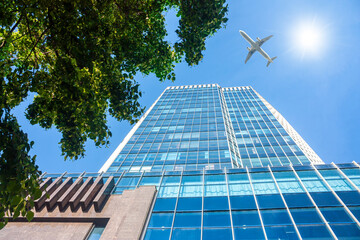 A modern office skyscraper and white passenger airplane flying over this building